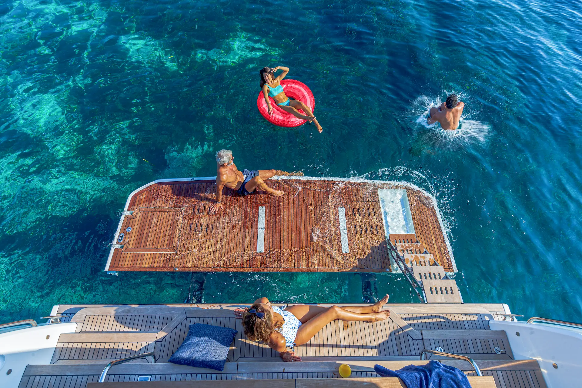 Familie geniet van de zon en het zwemmen rond een Beneteau-jacht op helderblauw water.