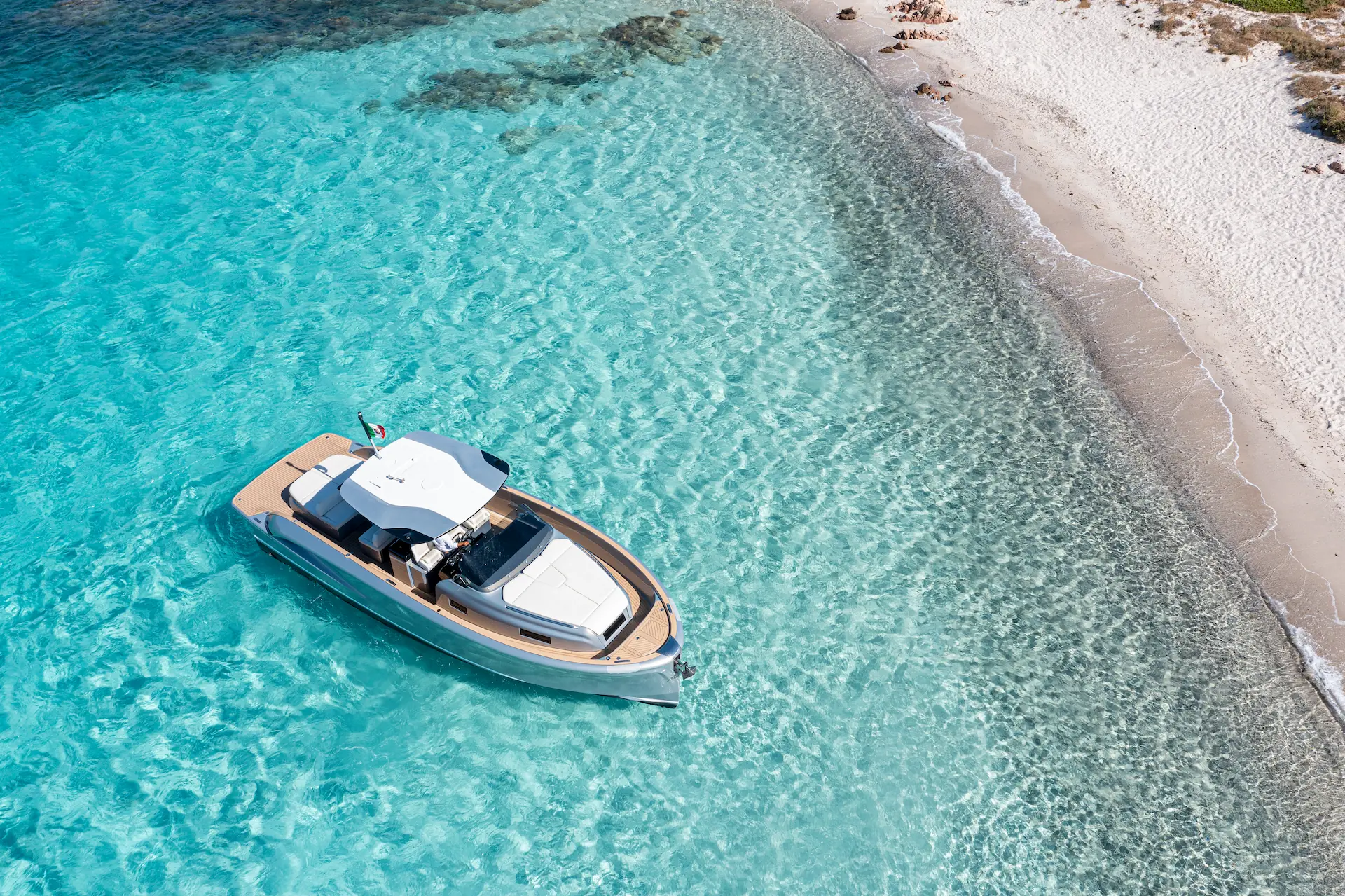 Luxe Solaris Power 40 Open jacht drijft op helderblauw water vlakbij een wit zandstrand.